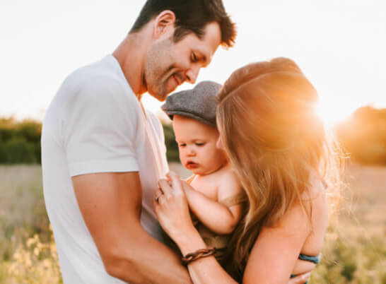 A family holding a baby in a field at sunset